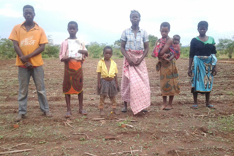 a Zambian family of seven standing in an empty farming plot