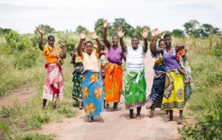 a group of women and young children standing on a road with their hands in the air