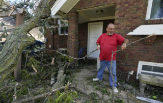 man red shirt removes fallen tree debris from his front yard