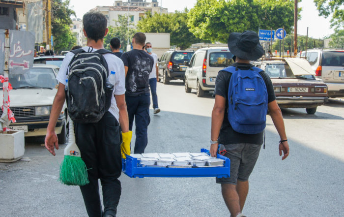 backs of men pictured carrying a pallet of meals to be given out in beirut