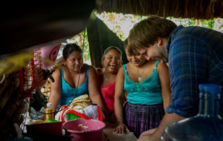 Three women and a man laugh while preparing a meal