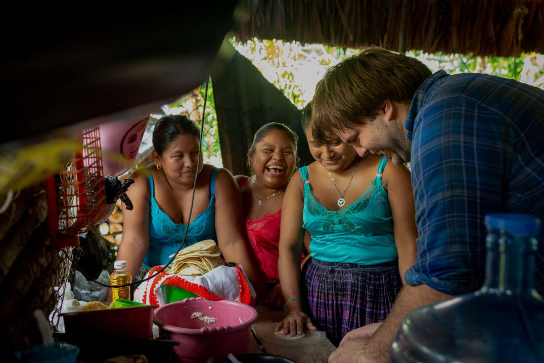 Three women and a man laugh while preparing a meal
