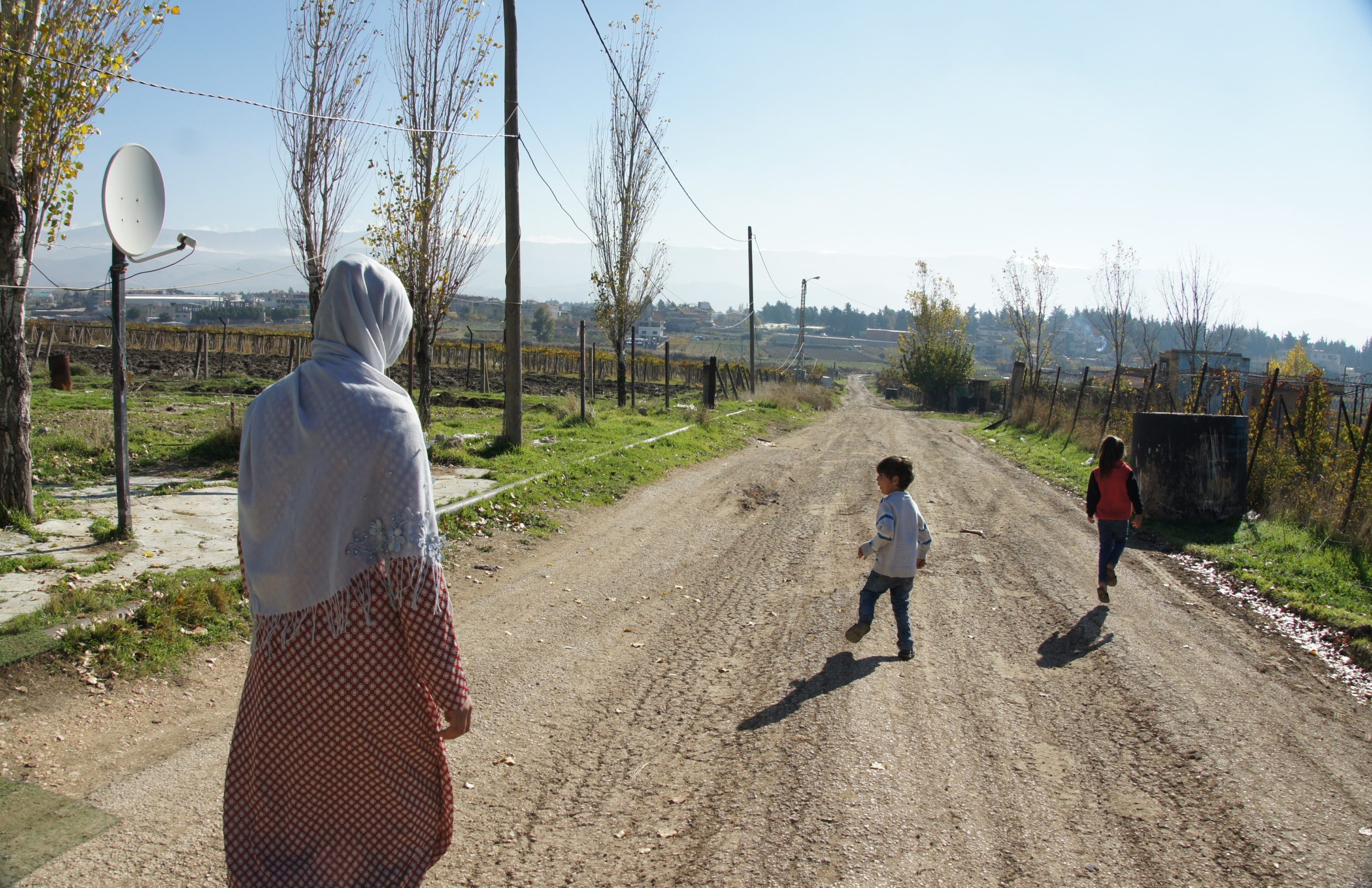 Syrian mother walks on a road as her two sons run ahead.