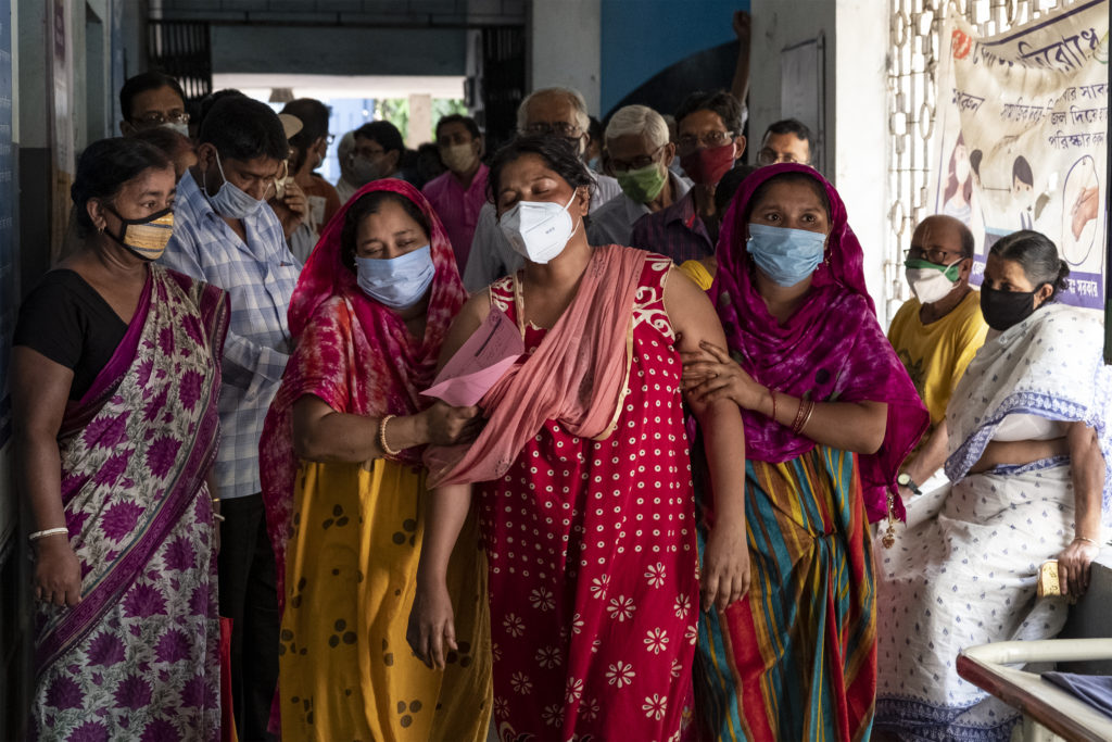 crowd of citizens with medical face masks ushering a woman through a hallway