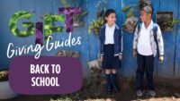 two smiling kids standing side-by-side with backpacks on with colorful words spelling out Gift Giving Guides Back to School